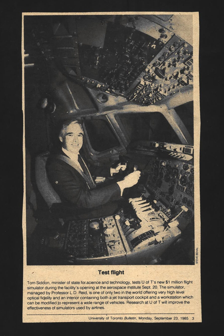 Newspaper clipping from University of Toronto Bulletin, Monday, September 23, 1985
Headline: Test flight
Photo: A suited man sits in the pilot’s chair of a flight simulator, surrounded by cockpit controls and instruments.
Caption: Tom Siddon, minister of state for science and technology, tests the University of Toronto’s new $1million flight simulator during the facility’s opening at the Institute for Aerospace Studies on September 20. The simulator, managed by Professor L.D. Reid, is one of only two in the world offering very high level optical fidelity and an interior containing both a jet transport cockpit and a workstation which can be modified to represent a wide range of vehicles. Research at the University of Toronto will improve the effectiveness of simulators used by airlines.