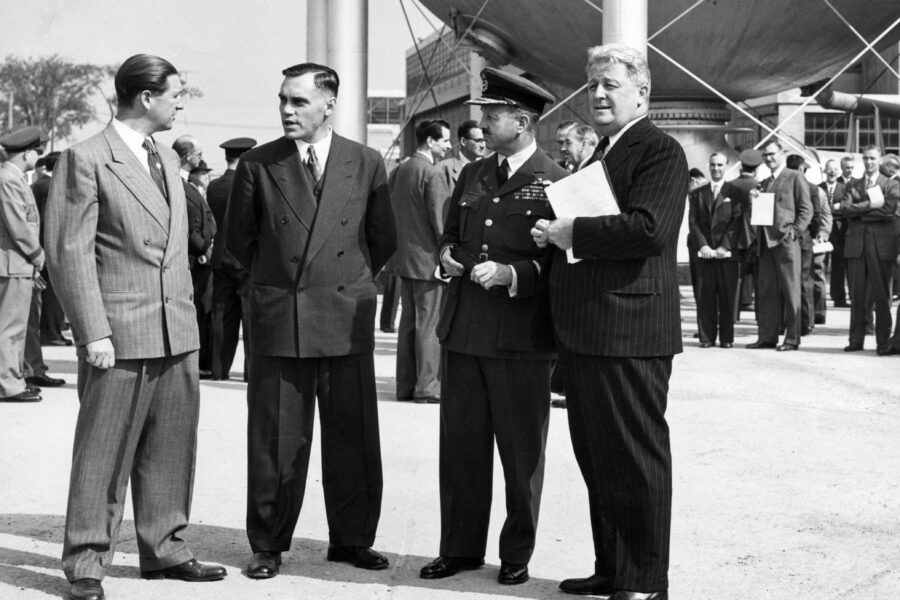 Four formally dressed men stand in front of an opening day crowd. In the background, part of the newly erected vacuum sphere and its surrounding building are visible.