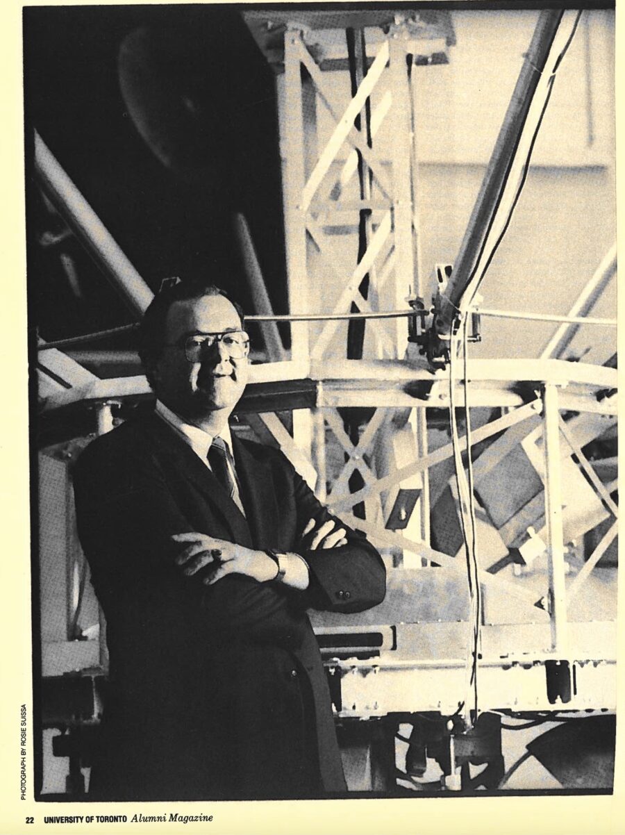 Professor Hughes, wearing a suit and tie, stands before the criss-crossing radial struts of Daisy.