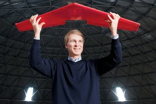 Professor David Zingg holds a red plane model aloft under the curved roof of the University of Toronto Institute for Aerospace Studies MARS Dome.