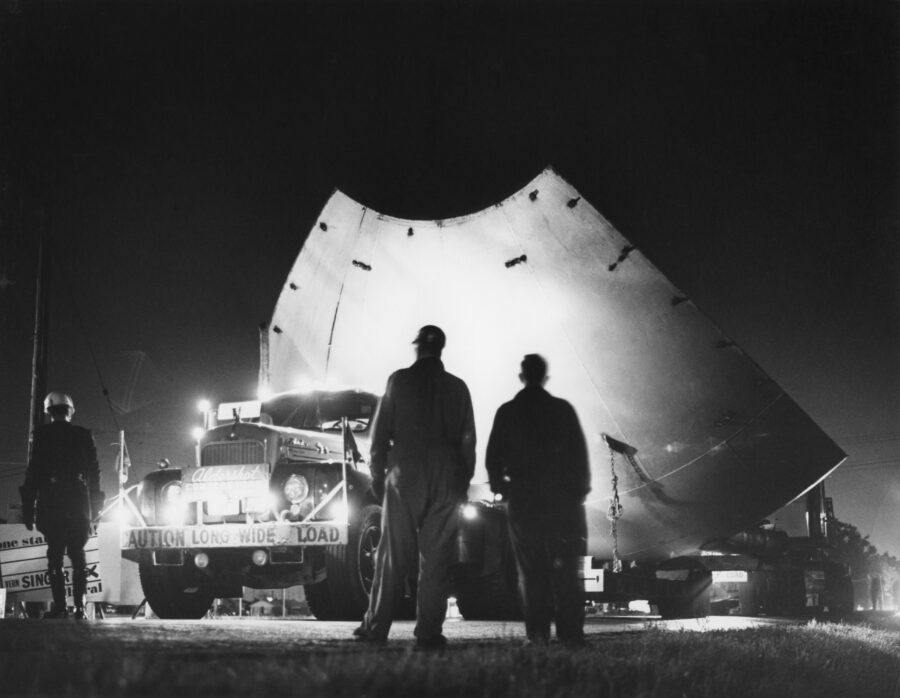 At night, two workmen and a police officer observe a transport truck loaded with a section of the giant metal sphere being transported to the new UTIAS location.