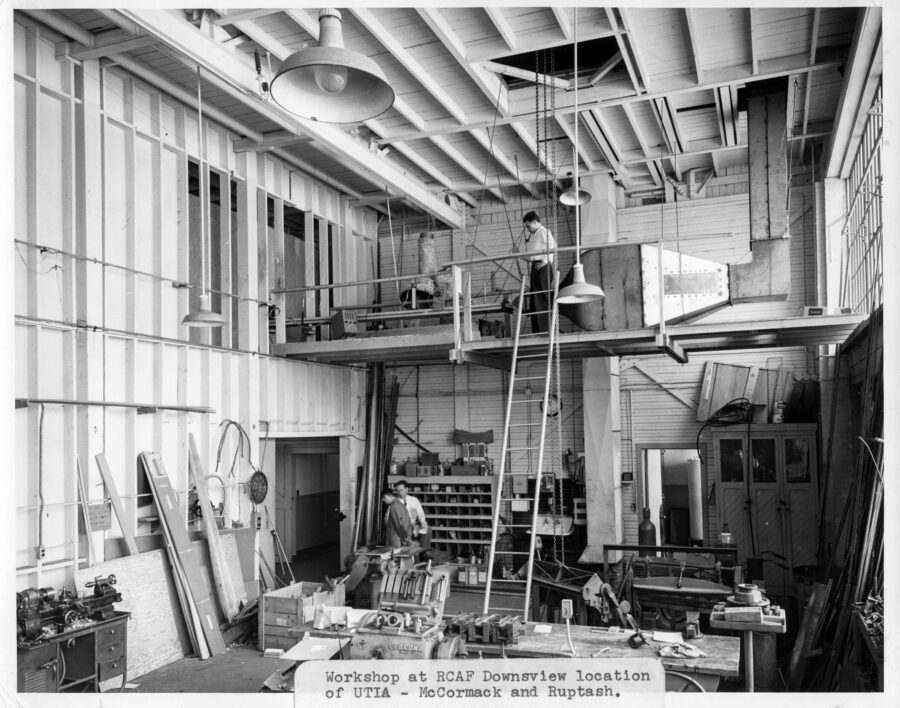 A long shot of a few men in the workshop at the Royal Canadian Air Force Downsview location of the Institute of Aerophysics. Scientific equipment is everywhere in the split level room.