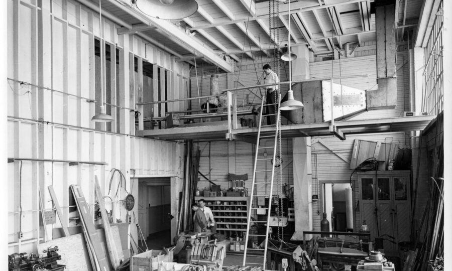 A long shot of a few men in the workshop at the Royal Canadian Air Force Downsview location of the Institute of Aerophysics. Scientific equipment is everywhere in the split level room.