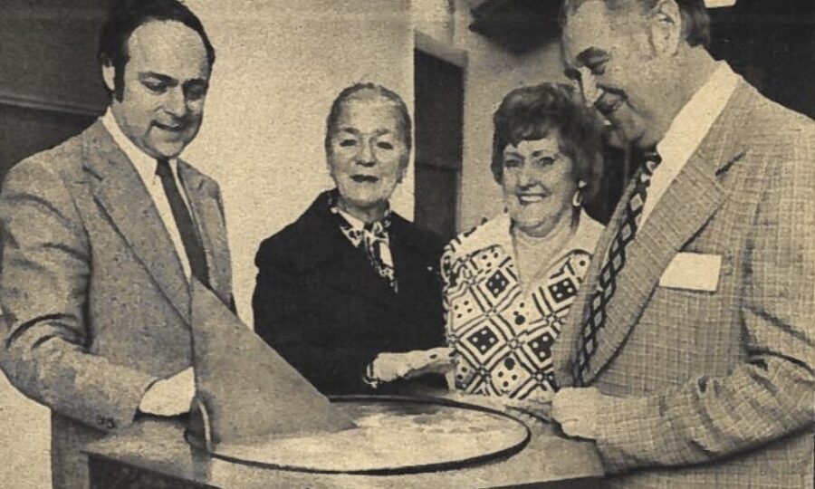 Two men and two women stand around an ornate sun dial.